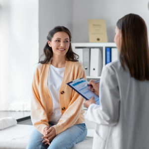 medicine, healthcare and people concept - female doctor with clipboard talking to smiling woman patient at hospital