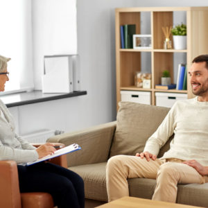 psychology, mental therapy and people concept - smiling senior woman psychologist with clipboard talking to young man patient at psychotherapy session